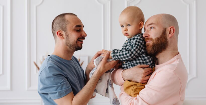 Same-sex parents lovingly holding their baby son indoors.