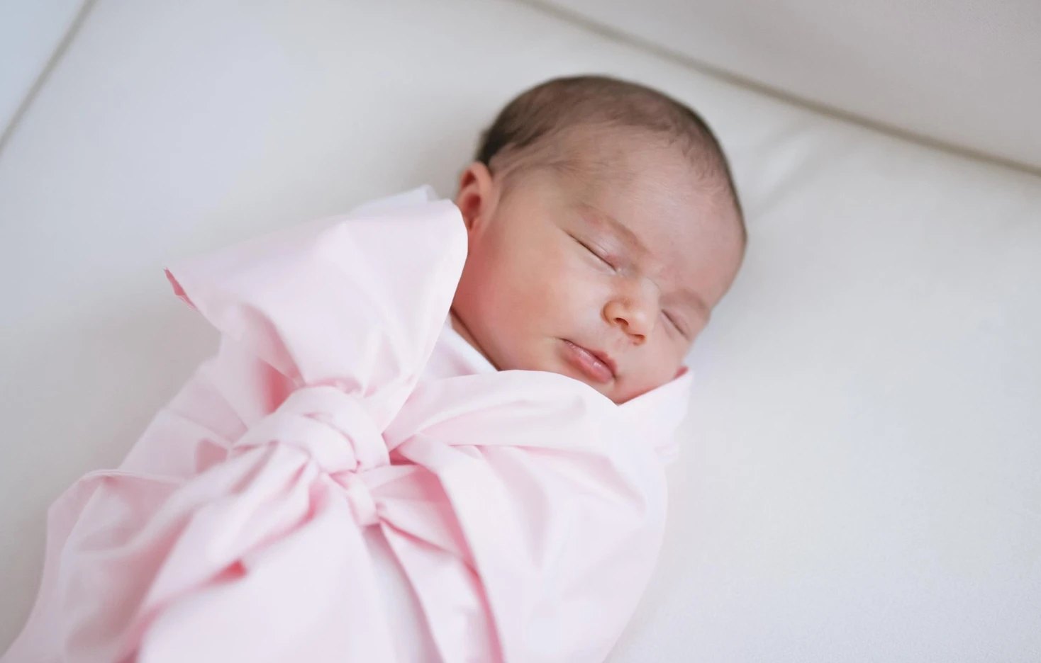 Newborn baby asleep in a soft pink wrap