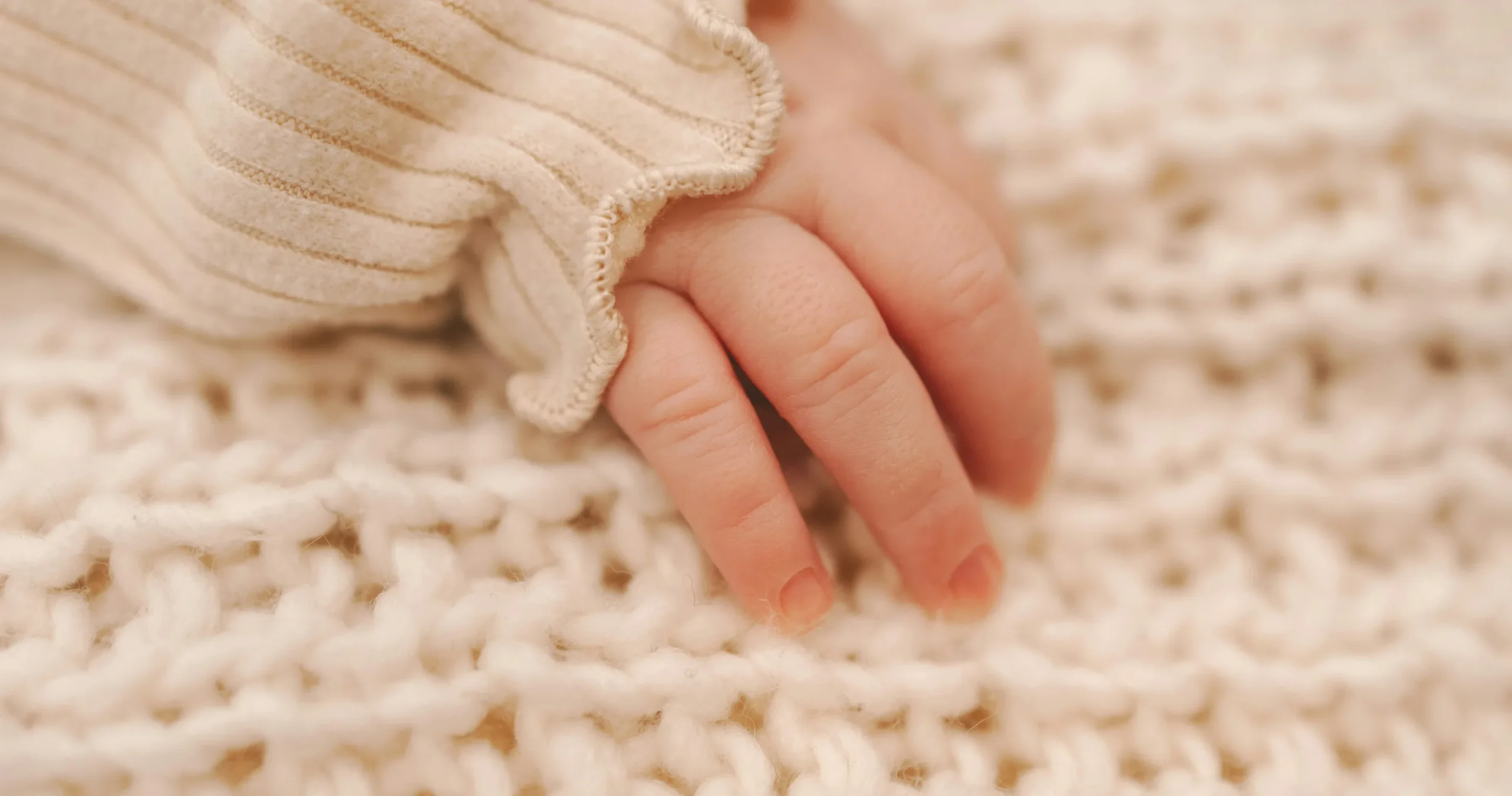 Newborn baby hand resting on a soft knitted blanket