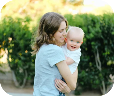 A woman holding her baby outdoors in front of a hedge