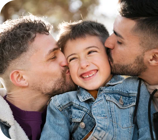 Two dads kissing their smiling child on the cheeks