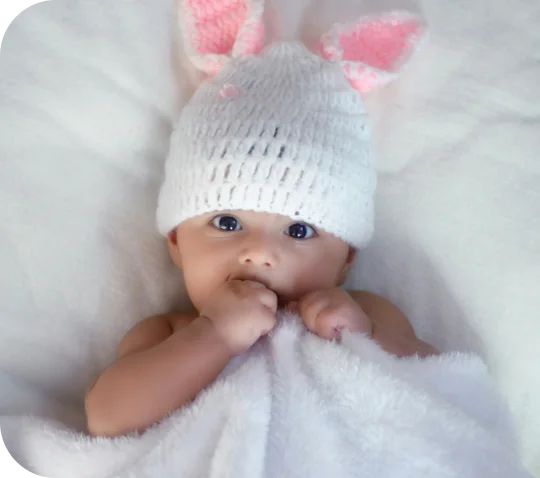 A newborn in a white bunny-ear hat wrapped in a soft towel