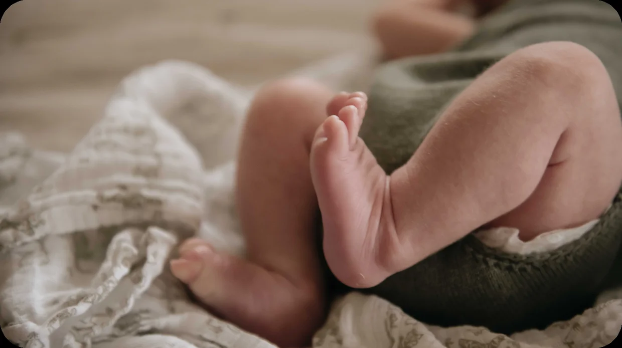 A newborn's legs curled over a soft muslin wrap