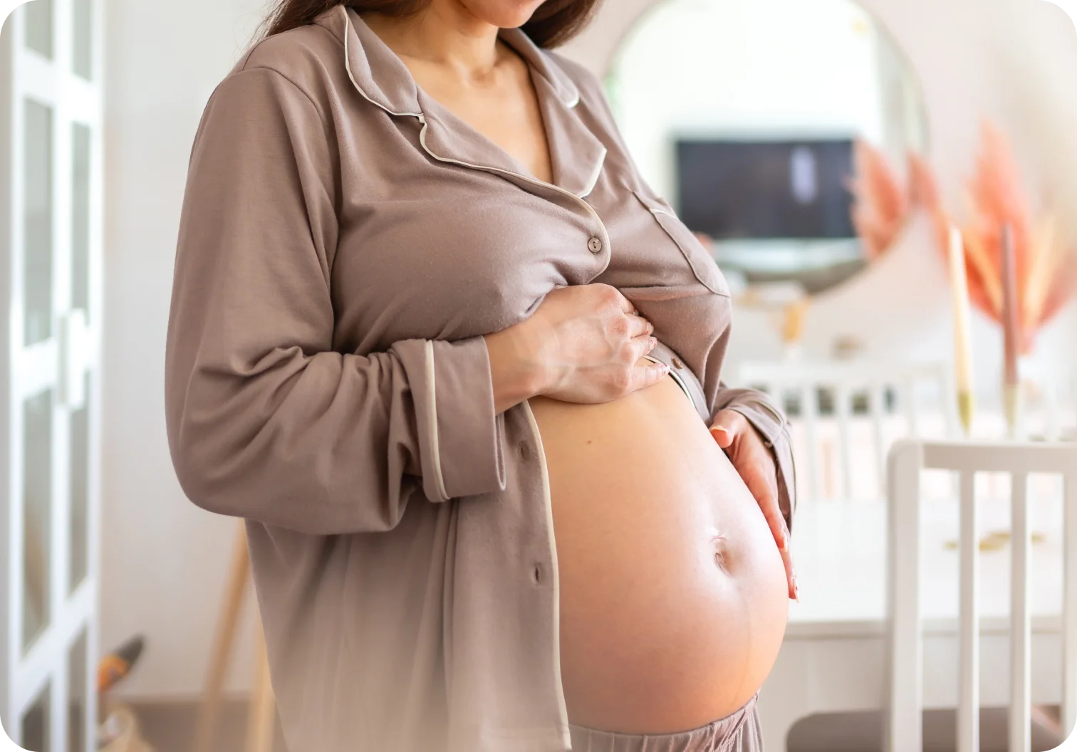 A pregnant woman in soft pajamas cradling her belly in a nursery