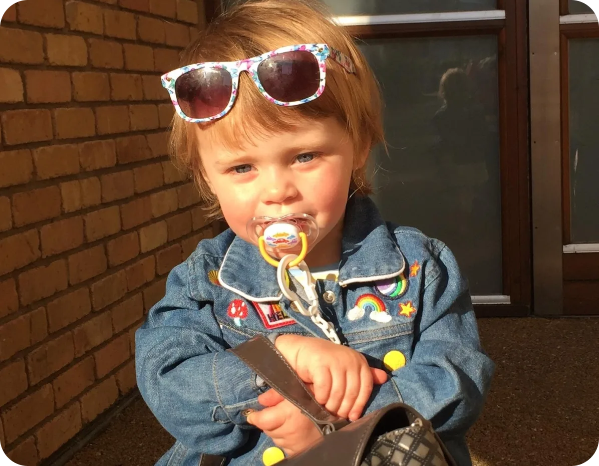 Toddler with sunglasses on her head smiling outside a brick house