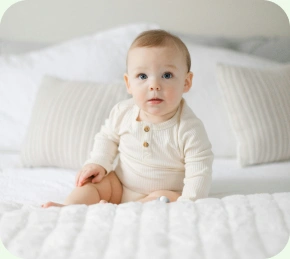 Baby sitting up on a white bed