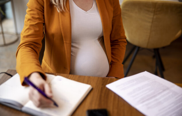 Pregnant woman in orange sweater writing in notebook