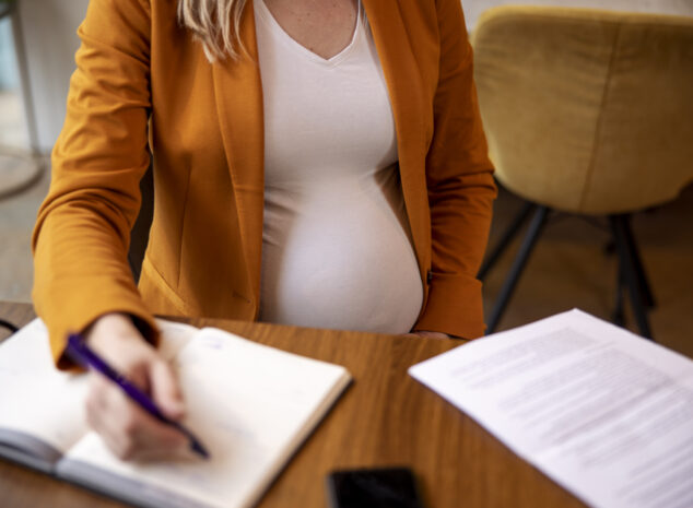 Pregnant woman in orange sweater writing in notebook