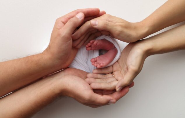Newborn baby's feet held gently by parents' hands against a white background.