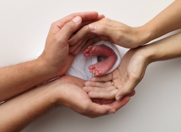 Newborn baby's feet held gently by parents' hands against a white background.