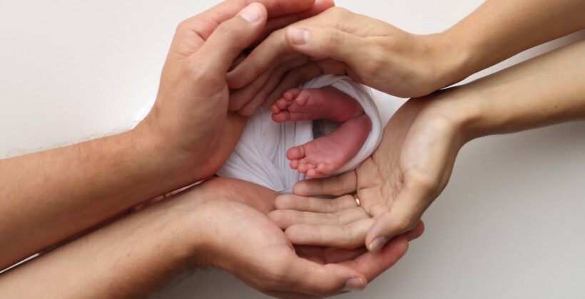 Newborn baby's feet held gently by parents' hands against a white background.
